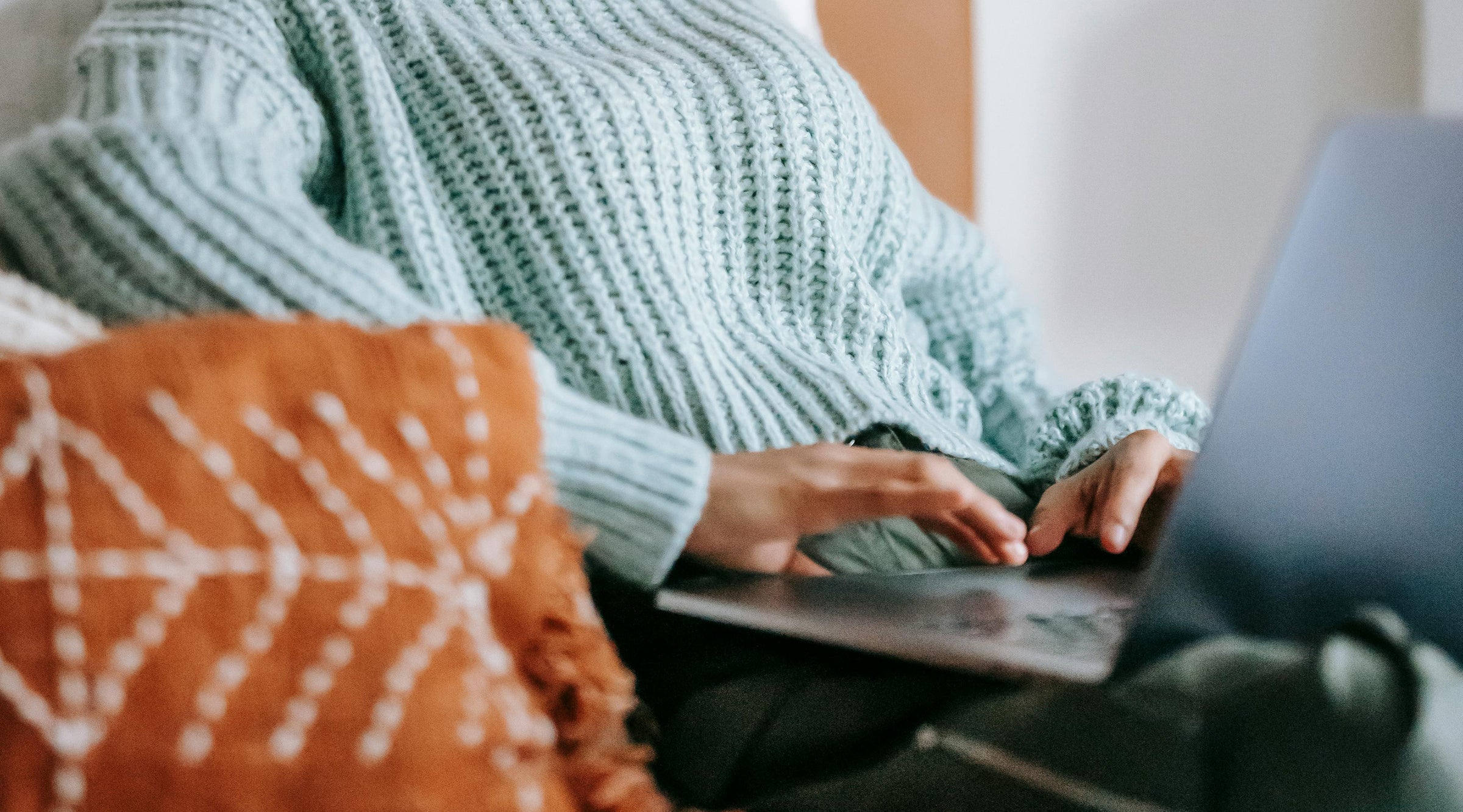 Una mujer recostada en una cama mientras trabaja en su laptop