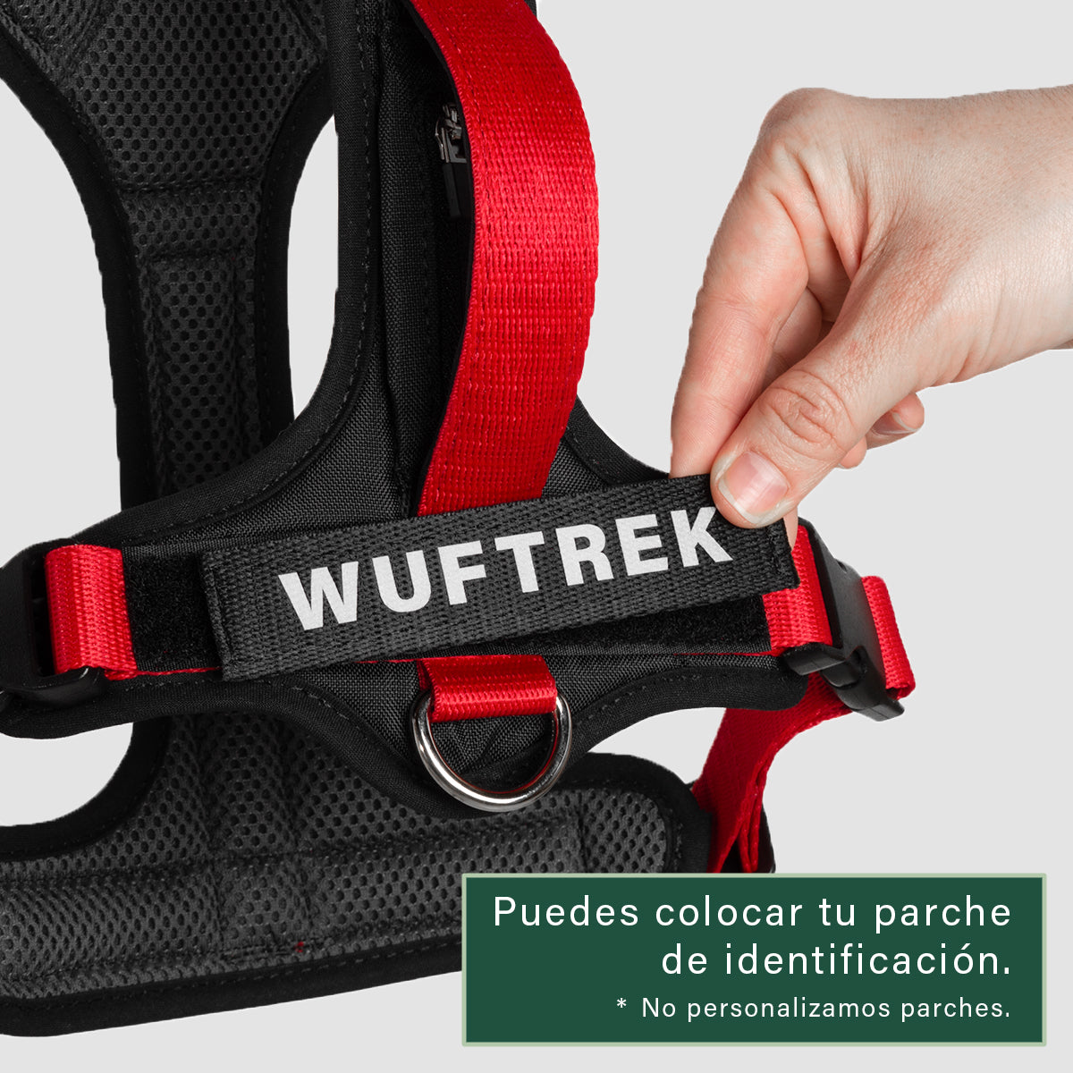 Una mano sosteniendo un parche de velcro con la palabra Wuftrek, poniendolo sobre una parche en un arnés color rojo con negro