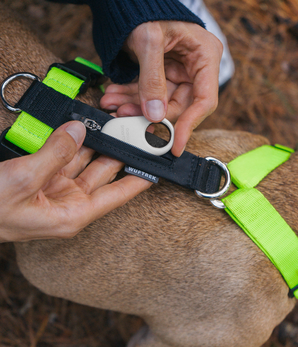Rear detail of the neon green TrekZero H-Series harness with two attachment rings and hands inserting a tracker into the rear pocket