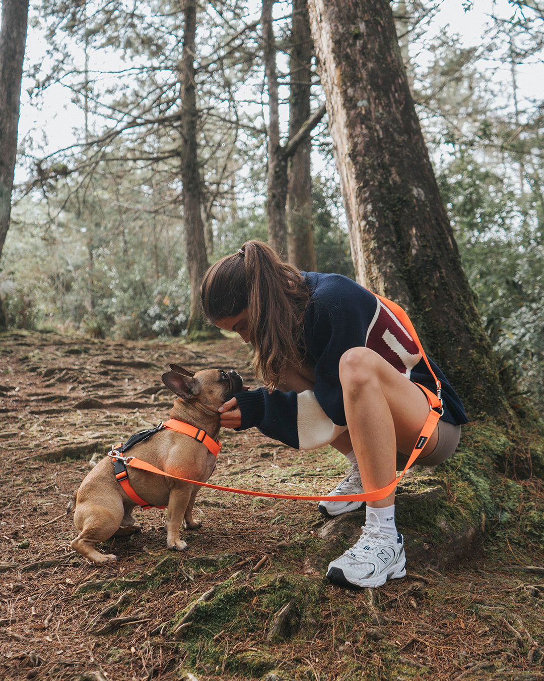 Una mujer junto a su mascota la cual tiene un arnés para perros color naranja